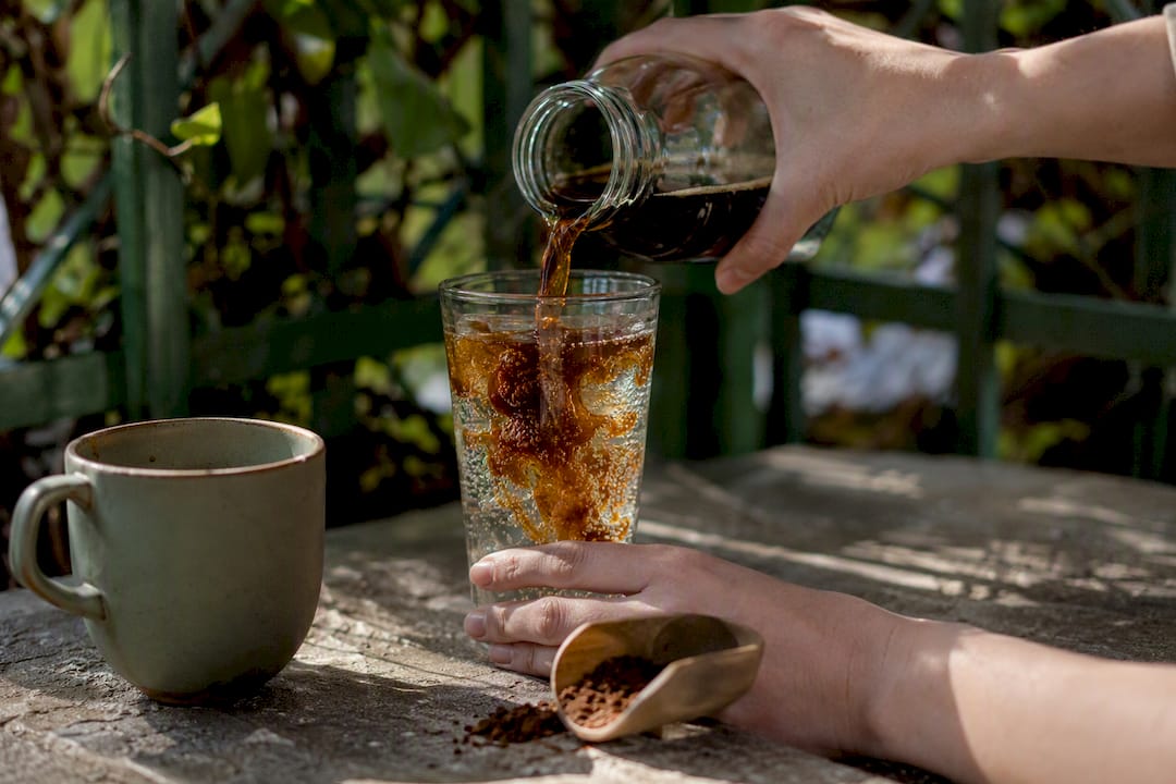 Hands pouring cold brew concentrate into glass